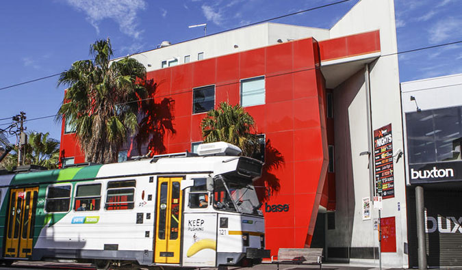 Red exterior of Base St. Kilda hostel with tram going by in front in Melbourne, Australia
