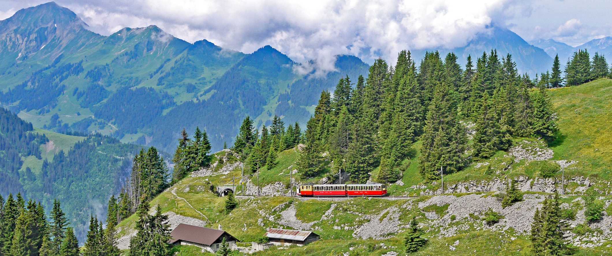 在瑞士因特拉肯少女峰铁路上，红色火车爬上陡峭的斜坡，背景是陡峭的山峰