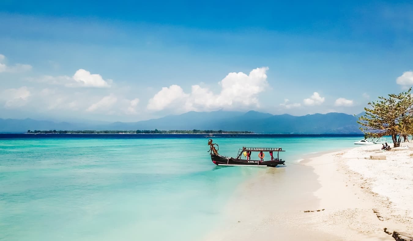 a gorgeous beach with a boat parked along the shore in the Gili Islands, Indonesia
