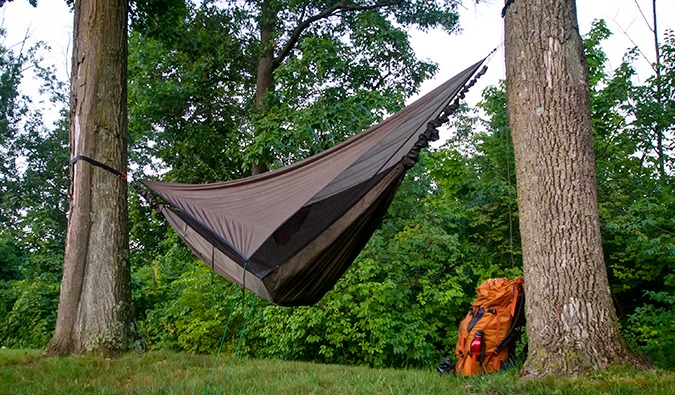 A hammock tied between two trees and a backpack sitting on the ground