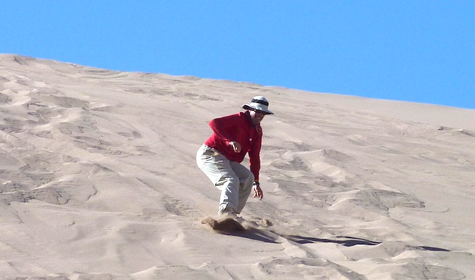 A 50 year old traveler sand boarding down a sand dune