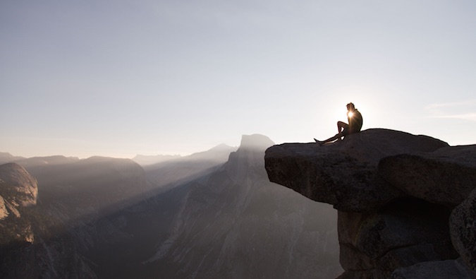 一个独自一人的旅行者坐在悬崖边，在日落时思考