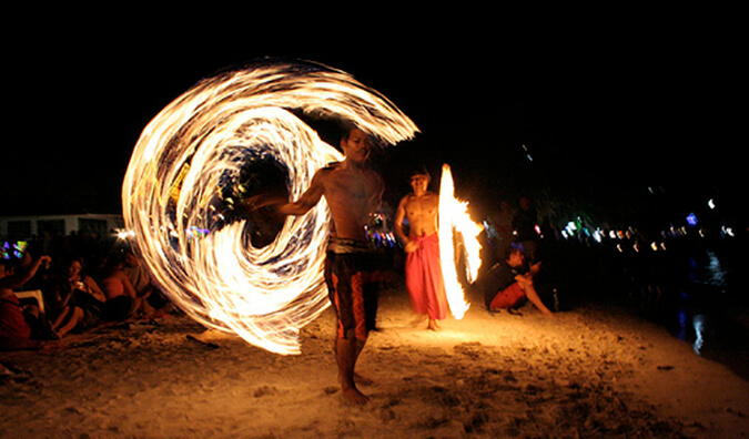 2 men dancing with fireballs on a beach at a full moon party