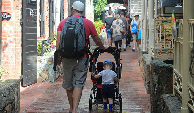 一位父亲推着婴儿车走在街上，婴儿车的后面站着一个蹒跚学步的孩子