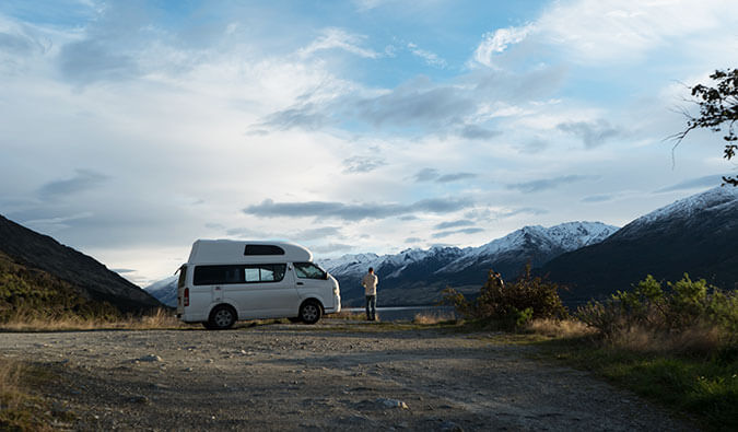一名男子站在一辆面包车旁，背景是新西兰的雪山