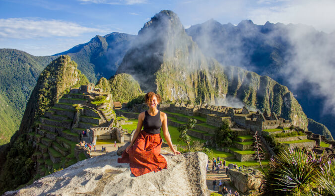 一名女子坐在前景中的一块岩石上，背景是马丘比丘