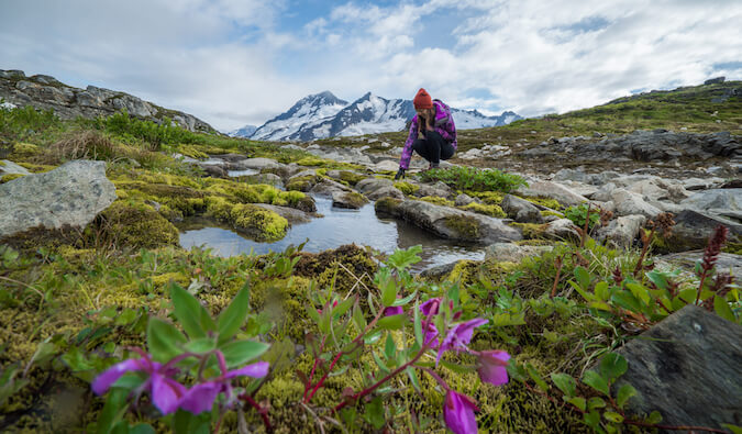 在阿拉斯加的一个女孩蹲下来触摸一块岩石的水花在前景和雪山的背景