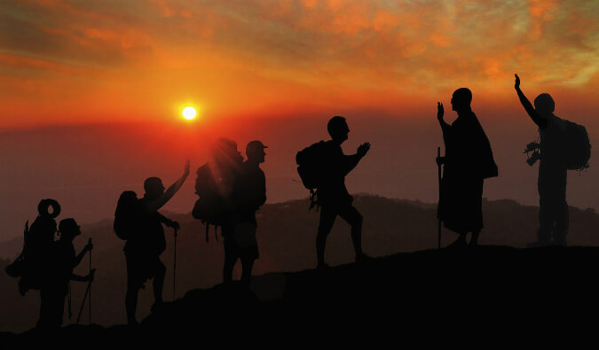 4个徒步旅行者有背包的爬行山被打招呼的山在顶部所有在红色日落的剪影