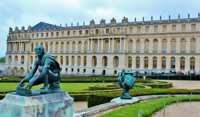 凡尔赛宫的照片摄于前景中宫殿对面的花园中，有一尊雕像，一个男人蹲着向远处看