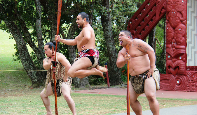 three Maori men in traditional dress performing a ritual dance