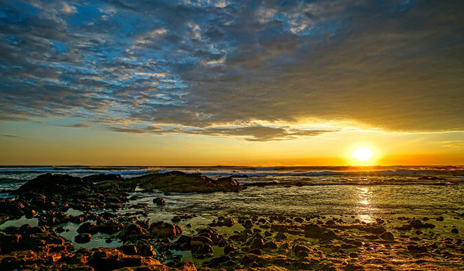 太阳落在布满岩石的海滩上，阳光反射在海面上