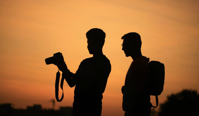 两名男子在看单反相机上日落时的剪影照片