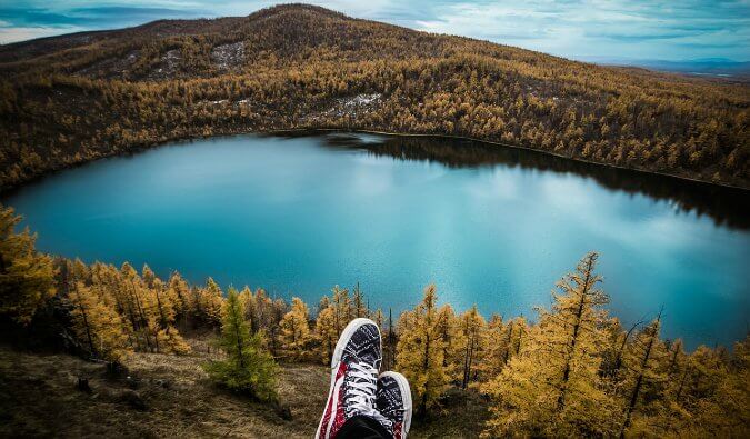 脚佩带运动鞋前面中心在树和绿叶周围的一个美丽的湖上方在背景中
