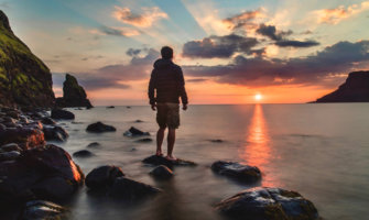一个独自旅行者站在海滩上，在日落时摆姿势拍一张忧郁的照片