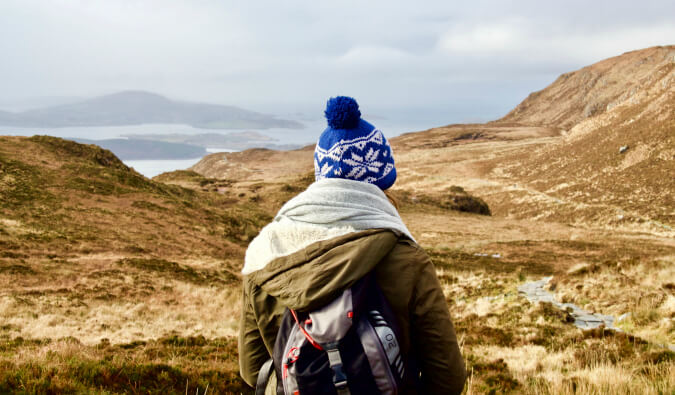 一个女人站在爱尔兰的山丘上，穿着暖和的冬衣，戴着一顶毡帽。