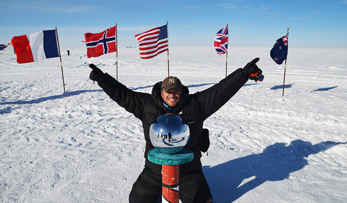 一名男子在一个被积雪覆盖的地方举起双臂庆祝自己的成就，身后是各国国旗