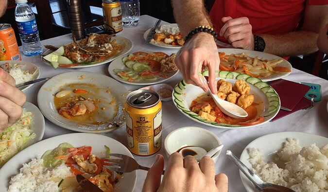 桌上摆着一盘盘的中国菜和啤酒罐，镜头中人们的手正准备吃饭
