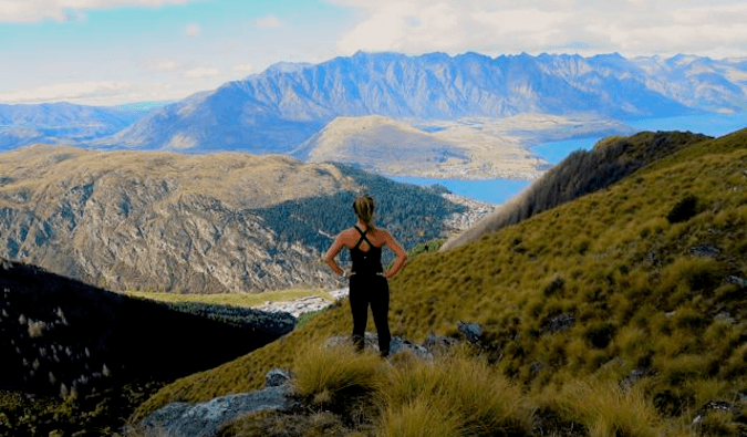 穿着运动服的女人站在高山上，双手叉腰俯视着风景