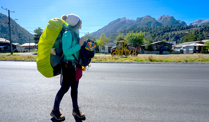 一个女背包客走在一条安静的街道上，远处有山