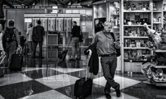 一张黑白照片，一个独自旅行者在机场看着他的手机