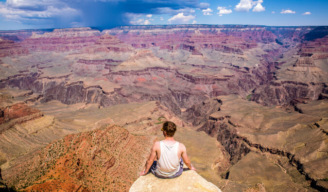 一个人坐在前面和后面中央被峡谷环绕的岩石上