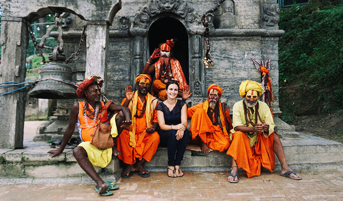 一名女子坐在印度一座寺庙外，5名男子穿着传统服装，脸上涂着彩绘