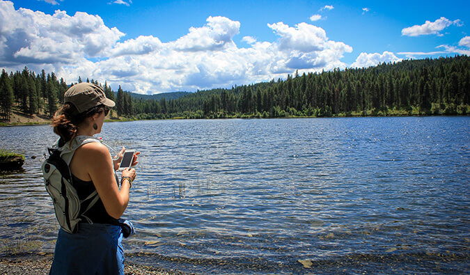 她的巧妙的电话的妇女站立在一个大风景湖旁边