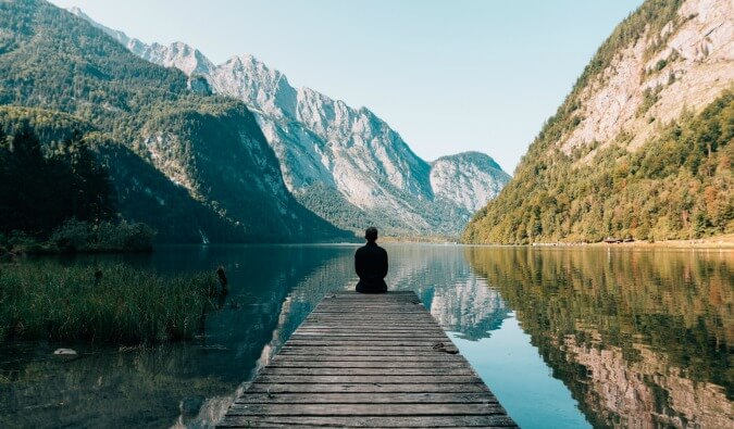 一名男子身穿黑色衣服，坐在被湖和山环绕的浮筒的一端