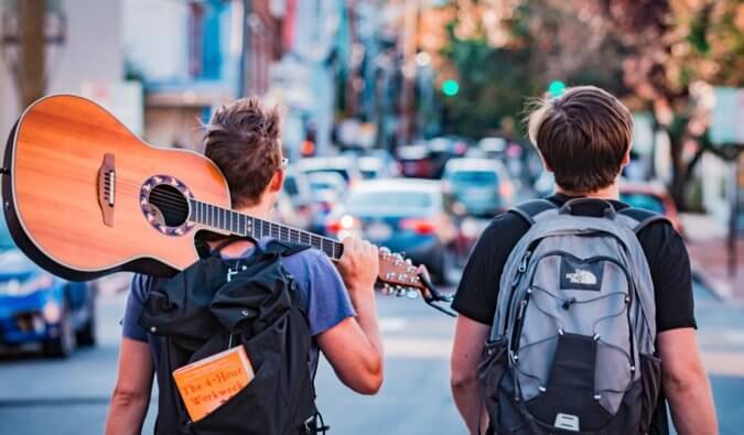 两个背包客走在街上，其中一个把吉他扛在肩上