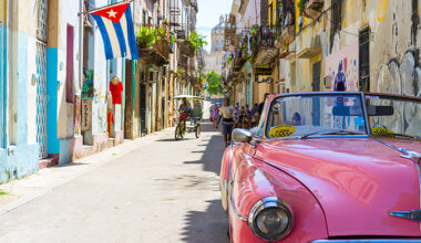 在哈瓦那五颜六色的街道上的经典粉红色汽车，与古巴旗子在背景中