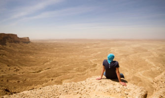 一个独自旅行者坐在沙特阿拉伯沙漠的悬崖上